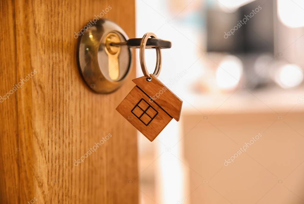 Key with house-shaped trinket in door lock, closeup