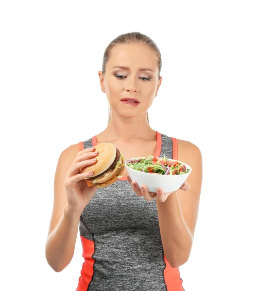运动妇女在新鲜蔬菜沙拉和汉堡包之间选择白色背景 — 图库照片
