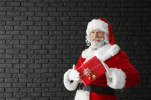 Weihnachtsmann Mit Geschenkbox Gegen Dunkle Ziegelwand — Stockfoto