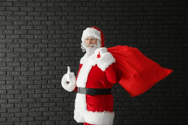 Kerstman Met Zak Vol Cadeaus Tegen Donkere Bakstenen Muur — Stockfoto