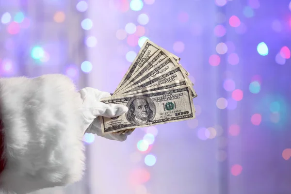 Рука Санта Клауса Держит Долларовые Купюры Против Разряженных Огней — стоковое фото