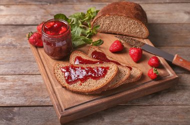 Kurulu ile dilim ekmek ve ahşap masa üzerinde lezzetli çilek reçeli