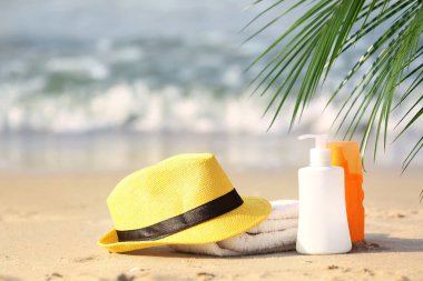 Kum deniz kenarında üzerinde havlu ve güneş koruyucu kozmetik ile şapka