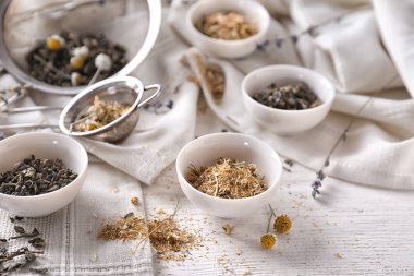 Kurutulmuş papatya ve beyaz tabloda çay yaprakları ile kase