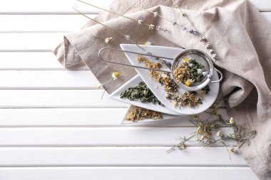 Elek ve kurutulmuş papatya ve beyaz ahşap tabloda çay yaprakları ile plakalar