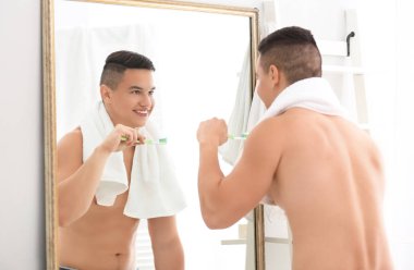 Genç adam banyoda dişlerini fırçalıyor.