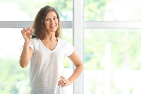 Happy young woman with key from her new house indoors