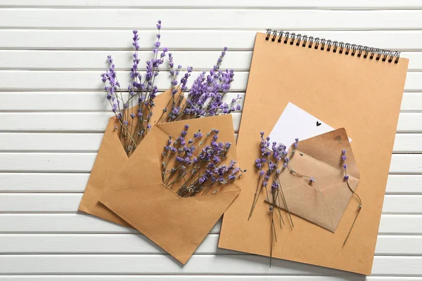 Mail envelopes with lavender flowers and notebook on white wooden background