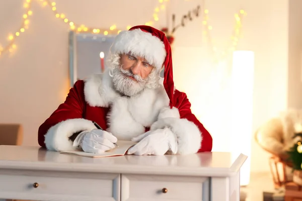 Санта Клаус Пишет Блокноте Сидя Столом Комнате Украшенной Рождество — стоковое фото