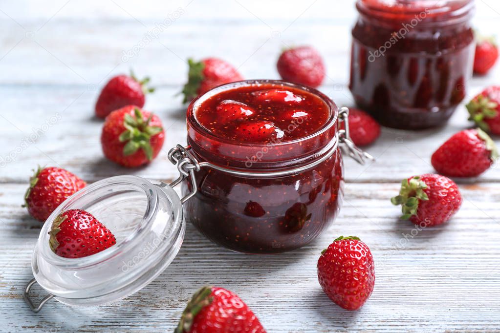 Glass jar with delicious strawberry jam on wooden table