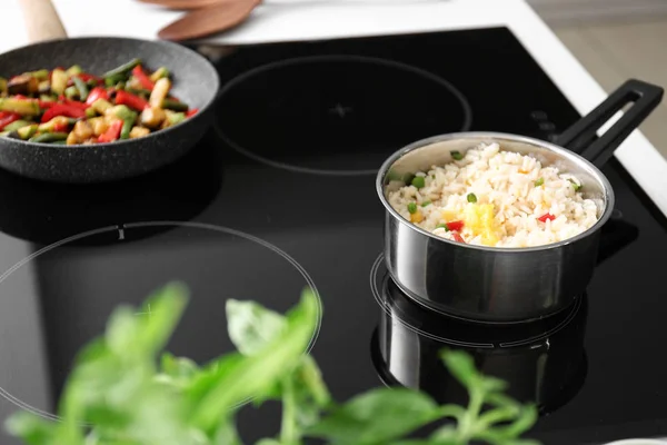 Saucepan with tasty rice and vegetables on stove in kitchen