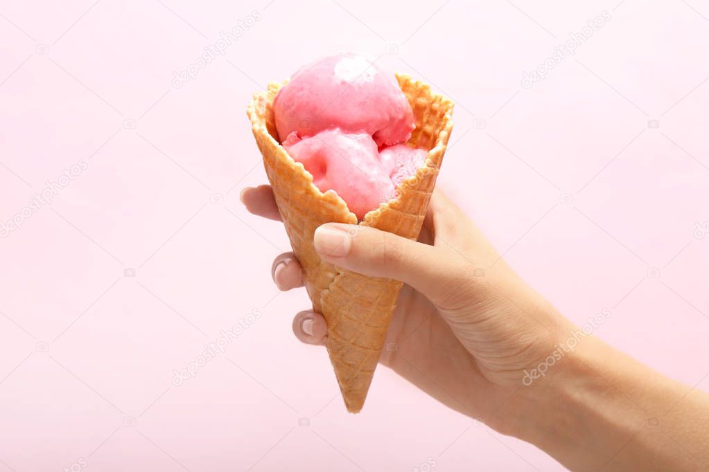 Woman holding waffle cone with delicious strawberry ice-cream on color background