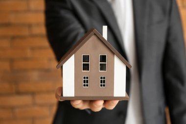 Emlakçı ile ev modeli tuğla duvar, closeup yakınındaki. İpotek kavramı