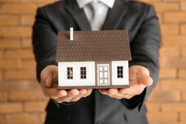 Emlakçı ile ev modeli tuğla duvar, closeup yakınındaki. İpotek kavramı