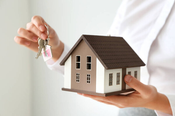 Real estate agent with house model and key on light background, closeup
