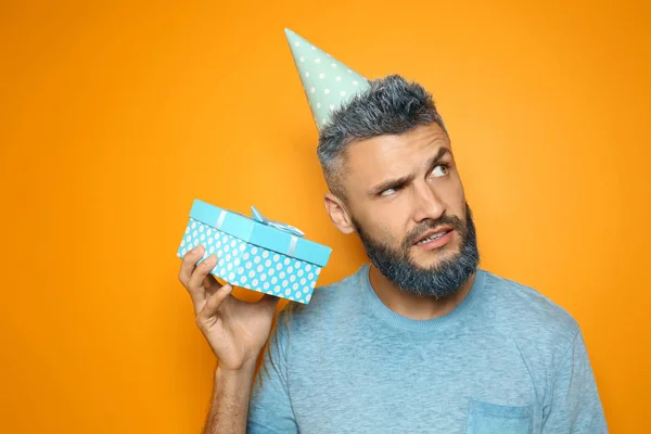Portrait of emotional man with Birthday gift on color background