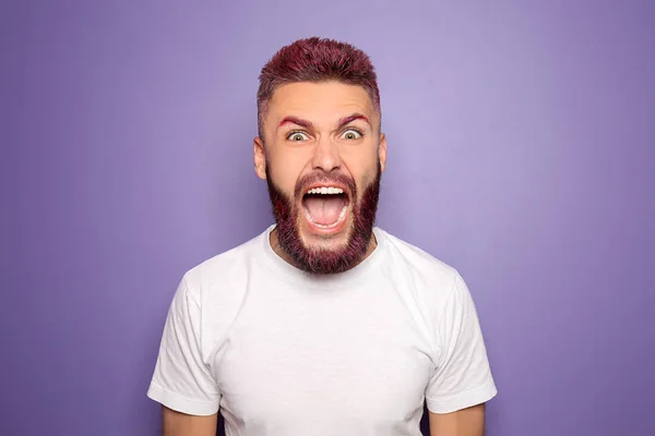 Portrait of angry screaming man with dyed hair and beard on color background