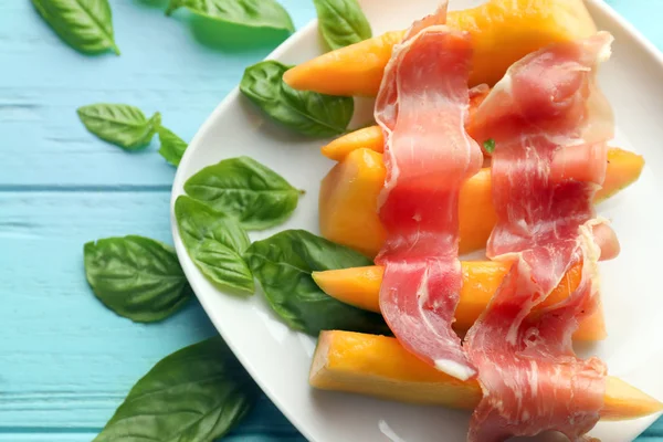 Plate with delicious melon and prosciutto on color table