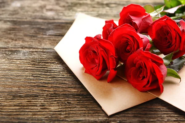 美丽的红玫瑰花束和信封上的木质背景 — 图库照片