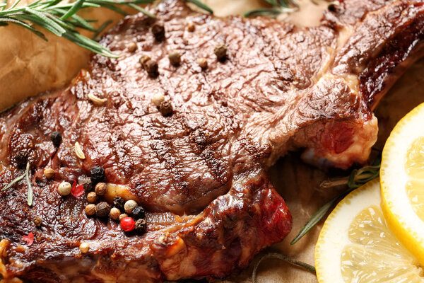 Tasty grilled steak with sliced lemon and spices on parchment, closeup