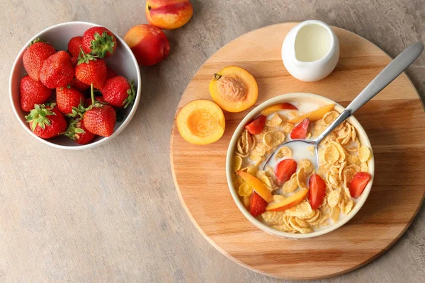 Tasty corn flakes with strawberry and peach in bowl on wooden board