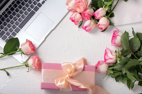 Beautiful roses, gift box and laptop on white table