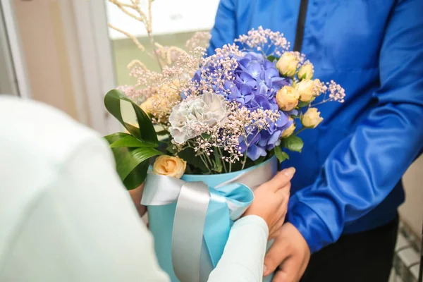 Young woman receiving gift box with beautiful flowers from delivery man