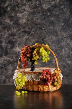 Wicker basket with fresh ripe grapes on dark grey background clipart