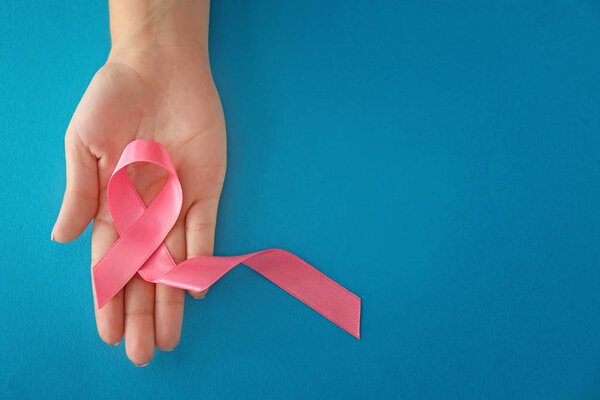 Woman holding pink ribbon on color background. Breast cancer concept