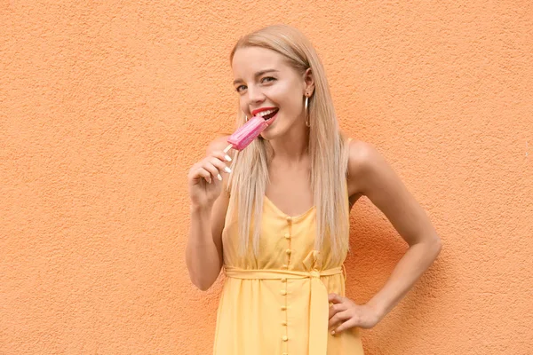 Beautiful young woman with ice cream near color wall