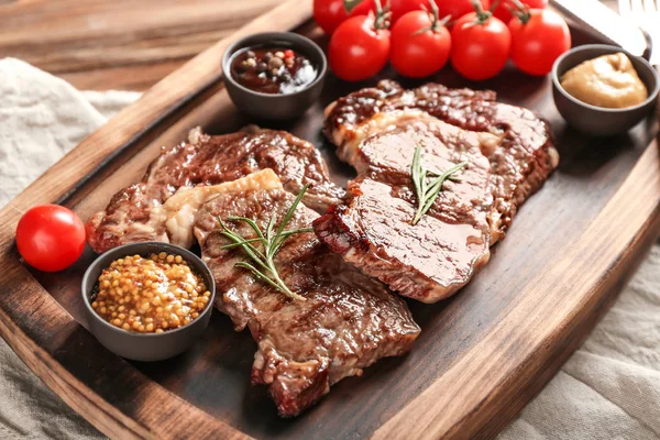 Delicious grilled steaks with sauces on wooden board