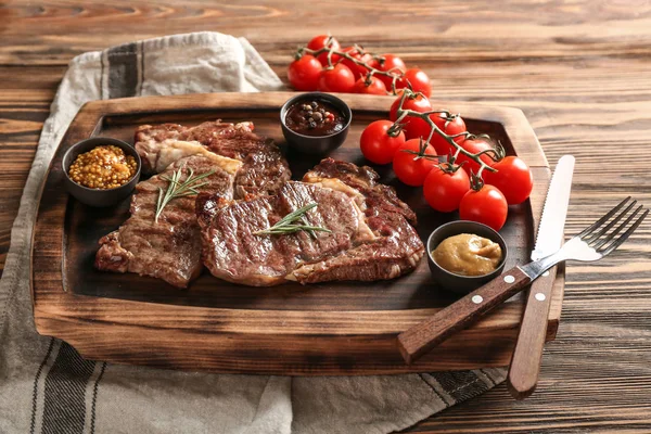 Delicious grilled steaks with sauces on wooden board