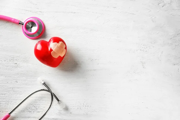 Medizinisches Stethoskop Und Rotes Herz Mit Gips Auf Weißem Holzgrund — Stockfoto