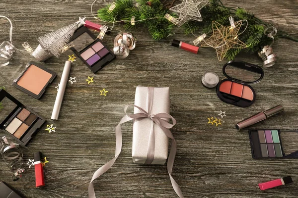 Set of cosmetics with Christmas present and decorations on wooden background