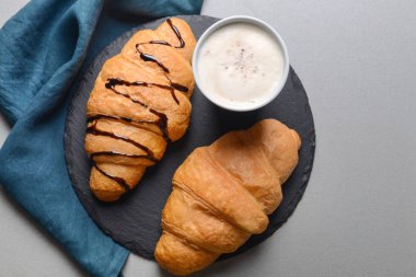 Kruvasan ve gri arka plan üzerinde içecek fincan ile kayrak plaka