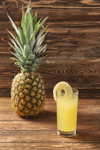 Pineapple and glass with fresh drink on wooden table