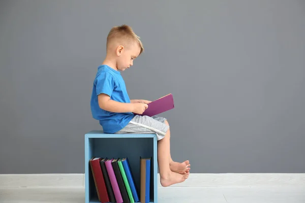 Милый Мальчик Читает Книжку Возле Серой Стены Помещении — стоковое фото