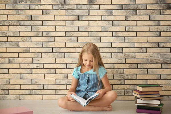 Cute Little Girl Reading Book Brick Wall Indoors — Stock Photo, Image