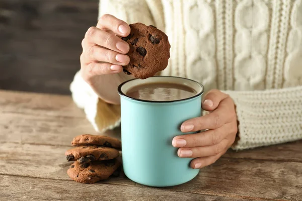 Woman with cup of tasty cocoa and cookies at wooden table, closeup