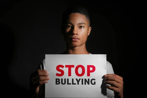暗い背景にいじめを停止テキストの紙のシートを保持しているアフリカ系アメリカ人の 代の少年 — ストック写真