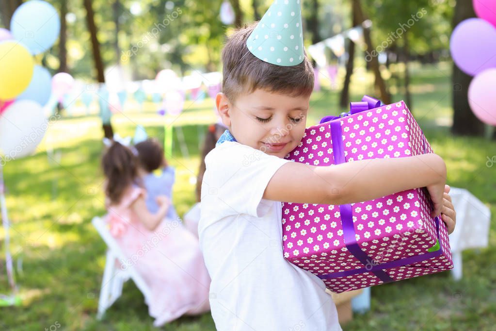 Cute little boy with gift box at birthday party outdoors