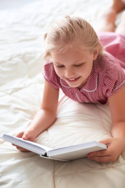 Sevimli küçük kız evde yatakta kitap okuma