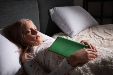 Sevimli küçük kız evde yatakta yatıyor kitapla