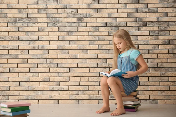 Cute Little Girl Reading Book Brick Wall Indoors — Stock Photo, Image