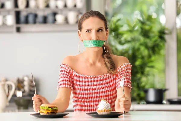 情绪化的女人 她的嘴巴周围有卷尺 厨房里不健康的食物 饮食理念 — 图库照片