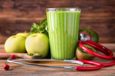 Lezzetli yeşil smoothie malzemeler ve ahşap masa üzerinde stetoskop ile bardak. Diyet kavramı