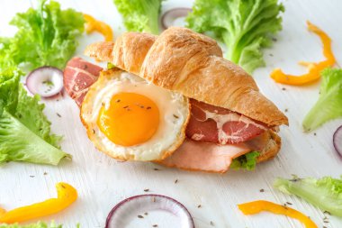 Beyaz ahşap masa üzerinde kızarmış yumurta ile lezzetli kruvasan sandviç