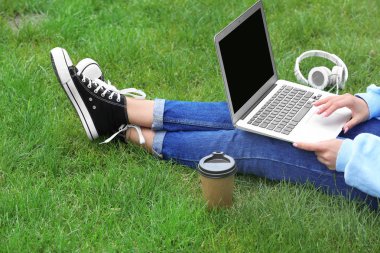 Park yeşil çimenlerin üzerinde dinlenme dizüstü bilgisayar ile genç kadın