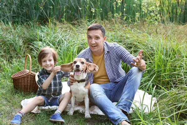 Father and his little son with dog resting in green park