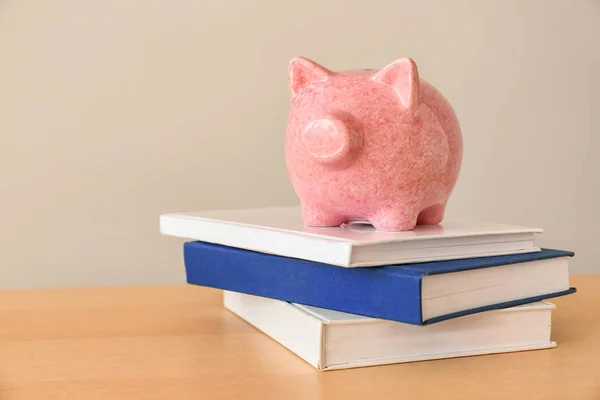 Piggy bank and stack of books on light wooden table